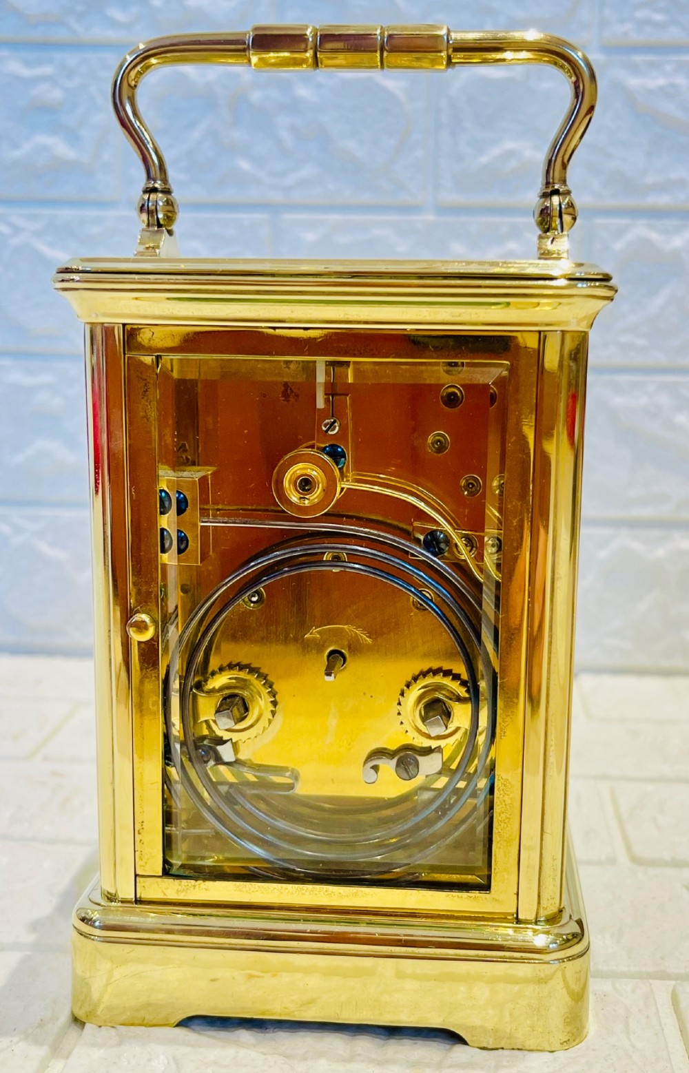 A rectangular French brass carriage clock featuring bevelled glass panels, a top carrying handle, an oval glass escapement window, and a white dial with Roman numerals. View VIII