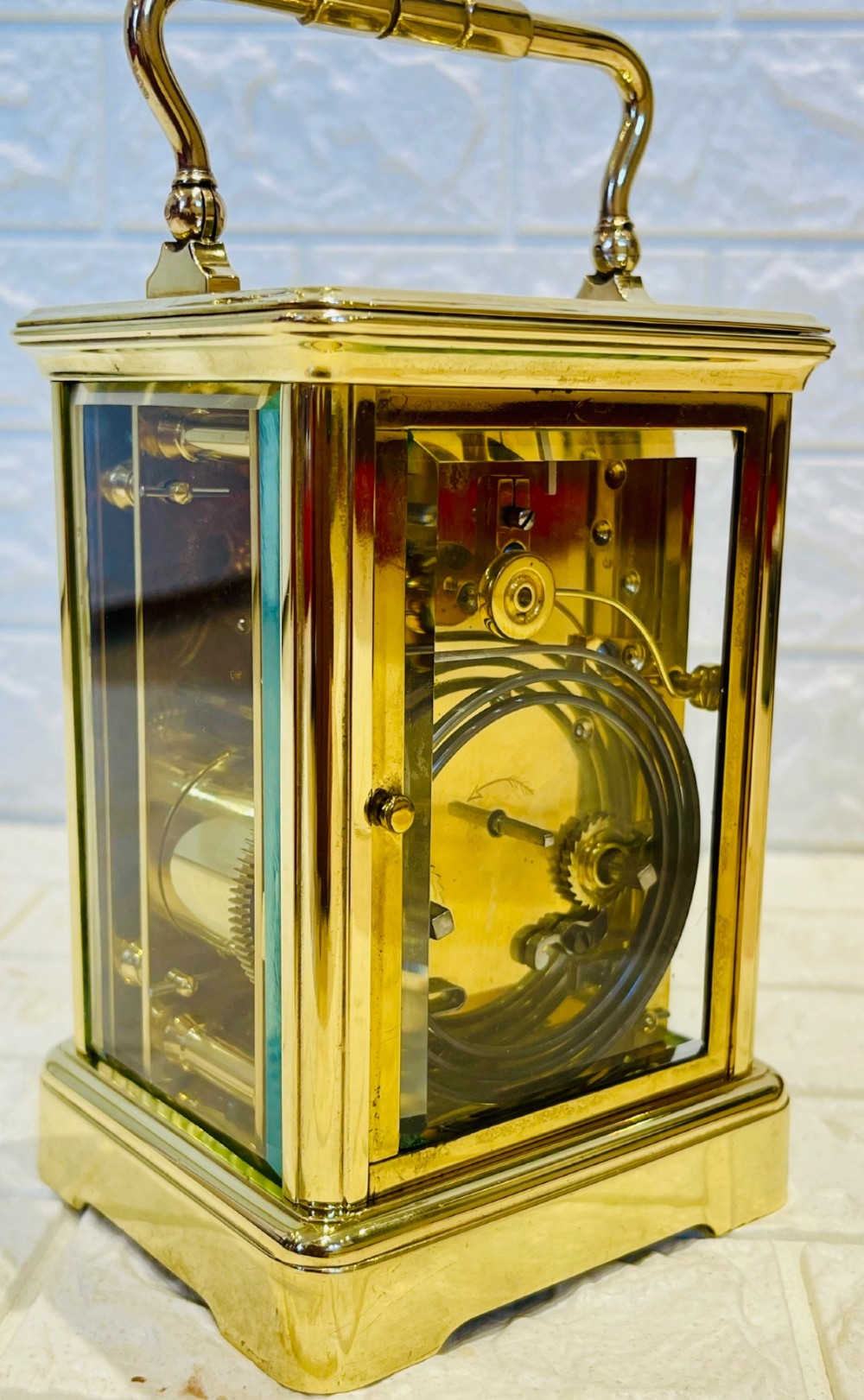 A rectangular French brass carriage clock featuring bevelled glass panels, a top carrying handle, an oval glass escapement window, and a white dial with Roman numerals. View IX