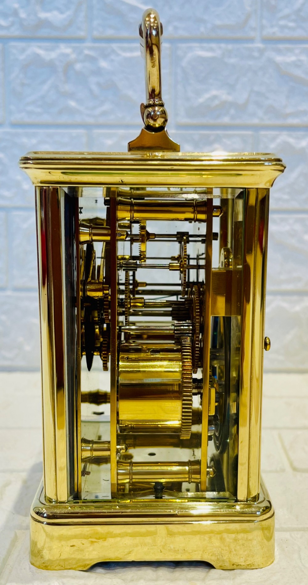 A rectangular French brass carriage clock featuring bevelled glass panels, a top carrying handle, an oval glass escapement window, and a white dial with Roman numerals. View X
