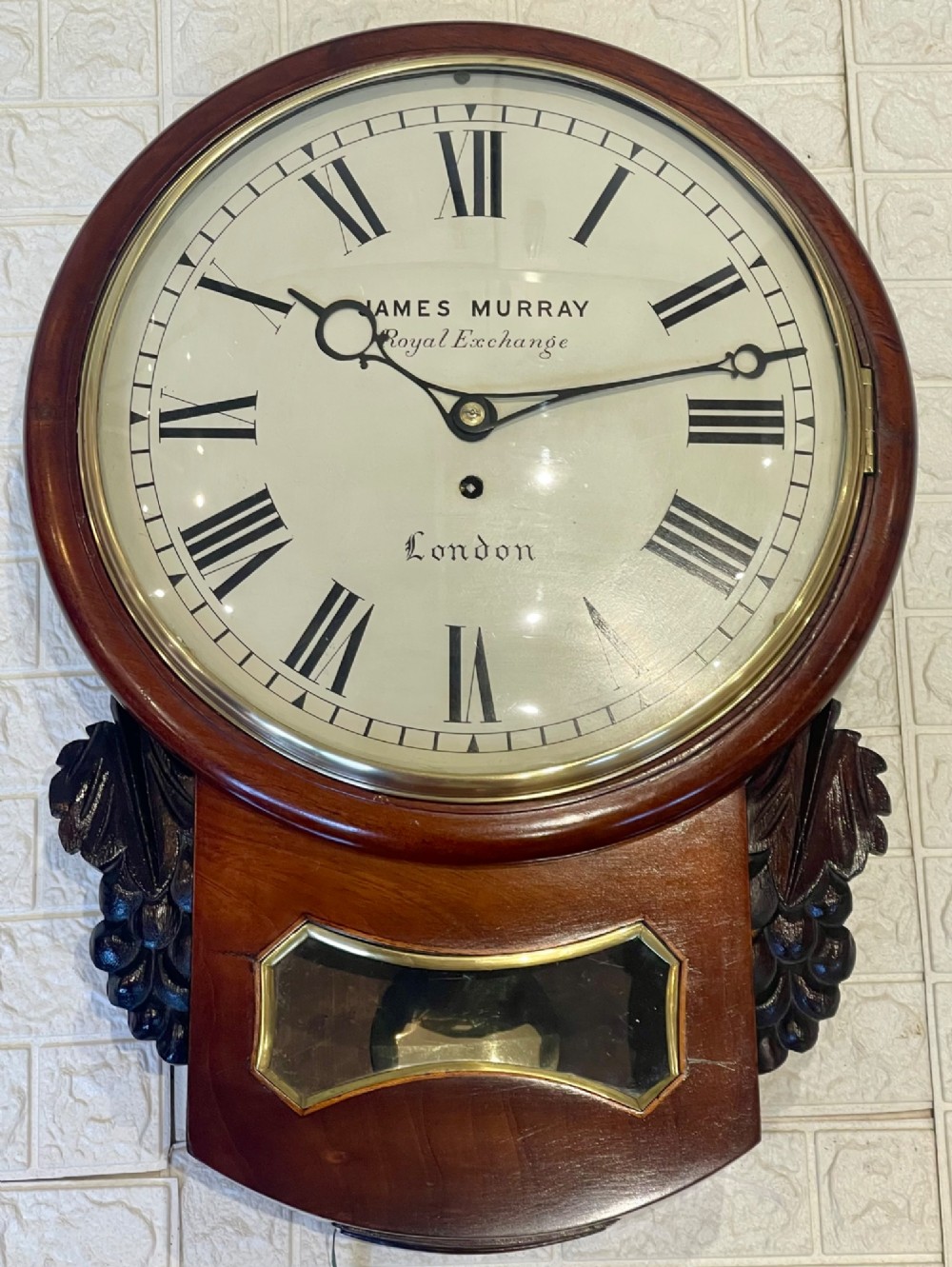 A mahogany drop dial fusee wall clock with a circular white dial signed James Murray London, black Roman numerals, a brass bezel, and carved side details. View IV