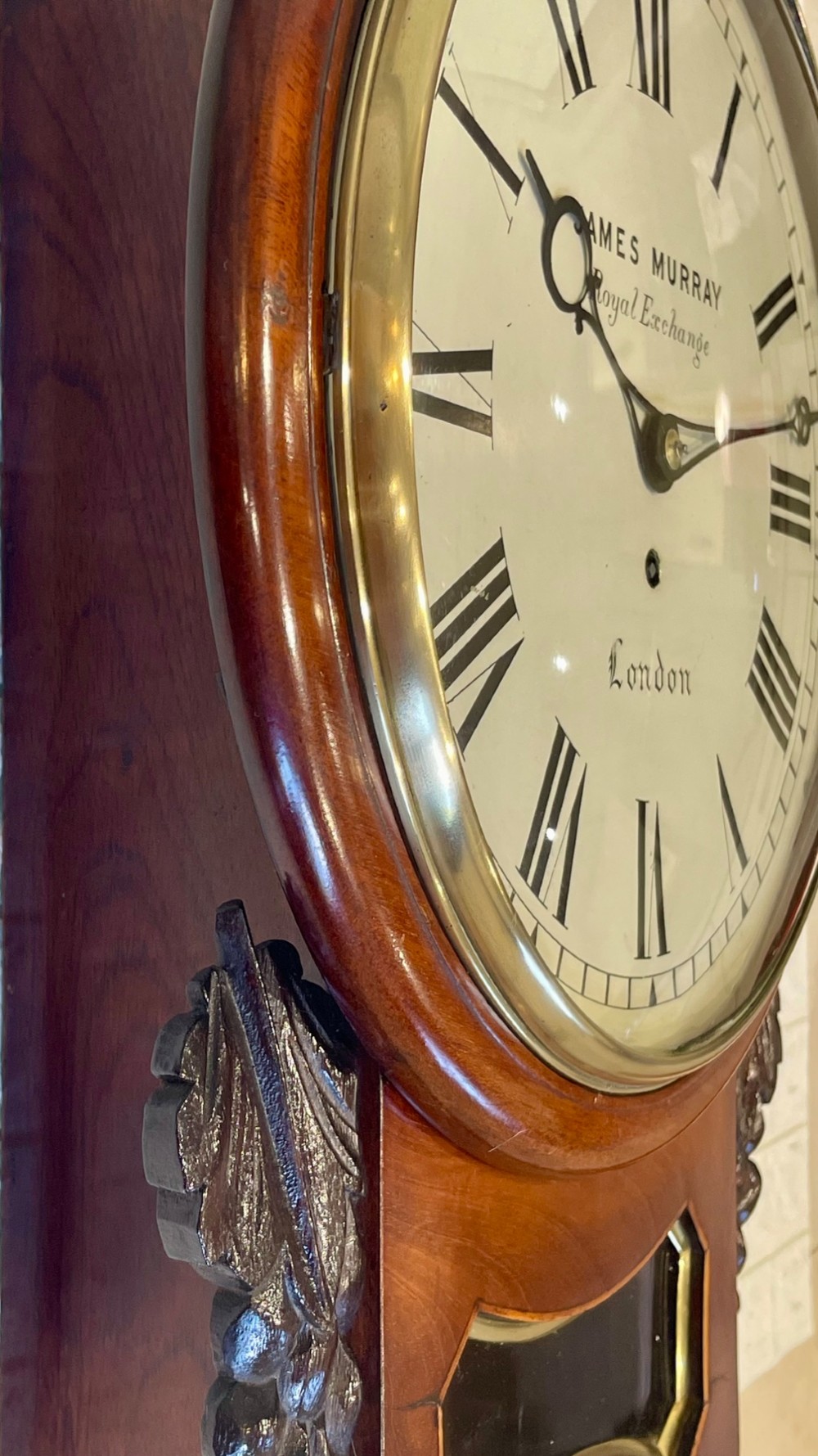 A mahogany drop dial fusee wall clock with a circular white dial signed James Murray London, black Roman numerals, a brass bezel, and carved side details. View V