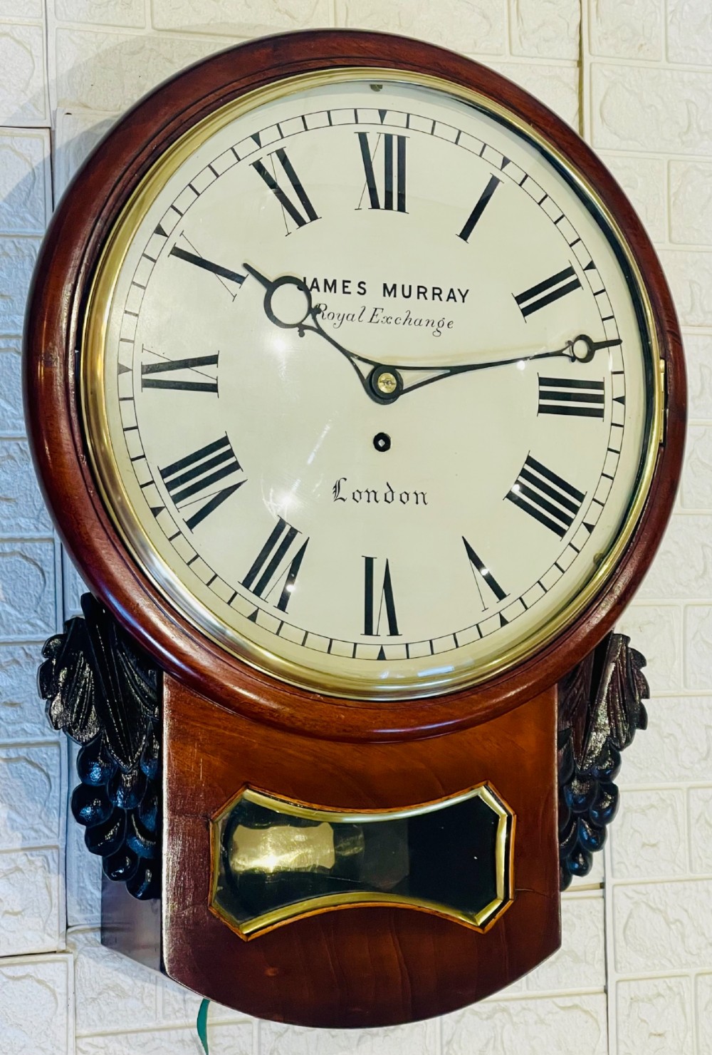 A mahogany drop dial fusee wall clock with a circular white dial signed James Murray London, black Roman numerals, a brass bezel, and carved side details. View IX