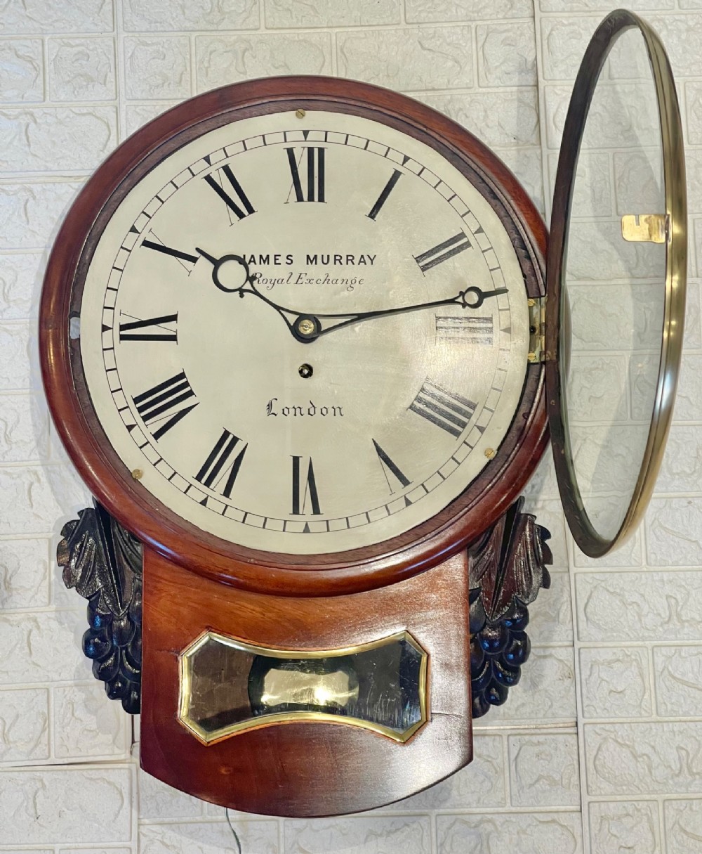 A mahogany drop dial fusee wall clock with a circular white dial signed James Murray London, black Roman numerals, a brass bezel, and carved side details. View XII
