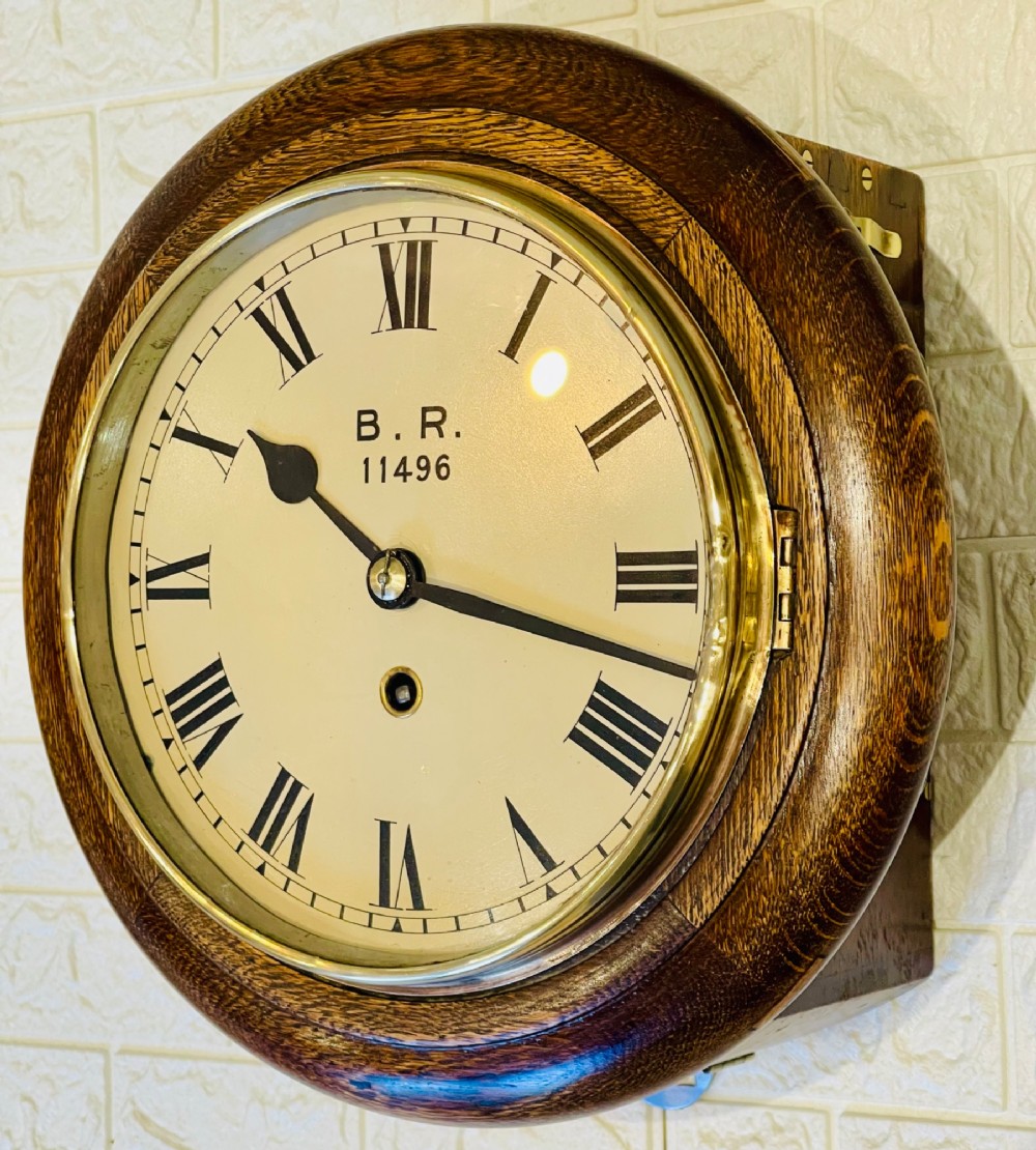 A circular oak wall clock featuring a brass bezel, Roman numerals, and British Rail markings printed on the dial.