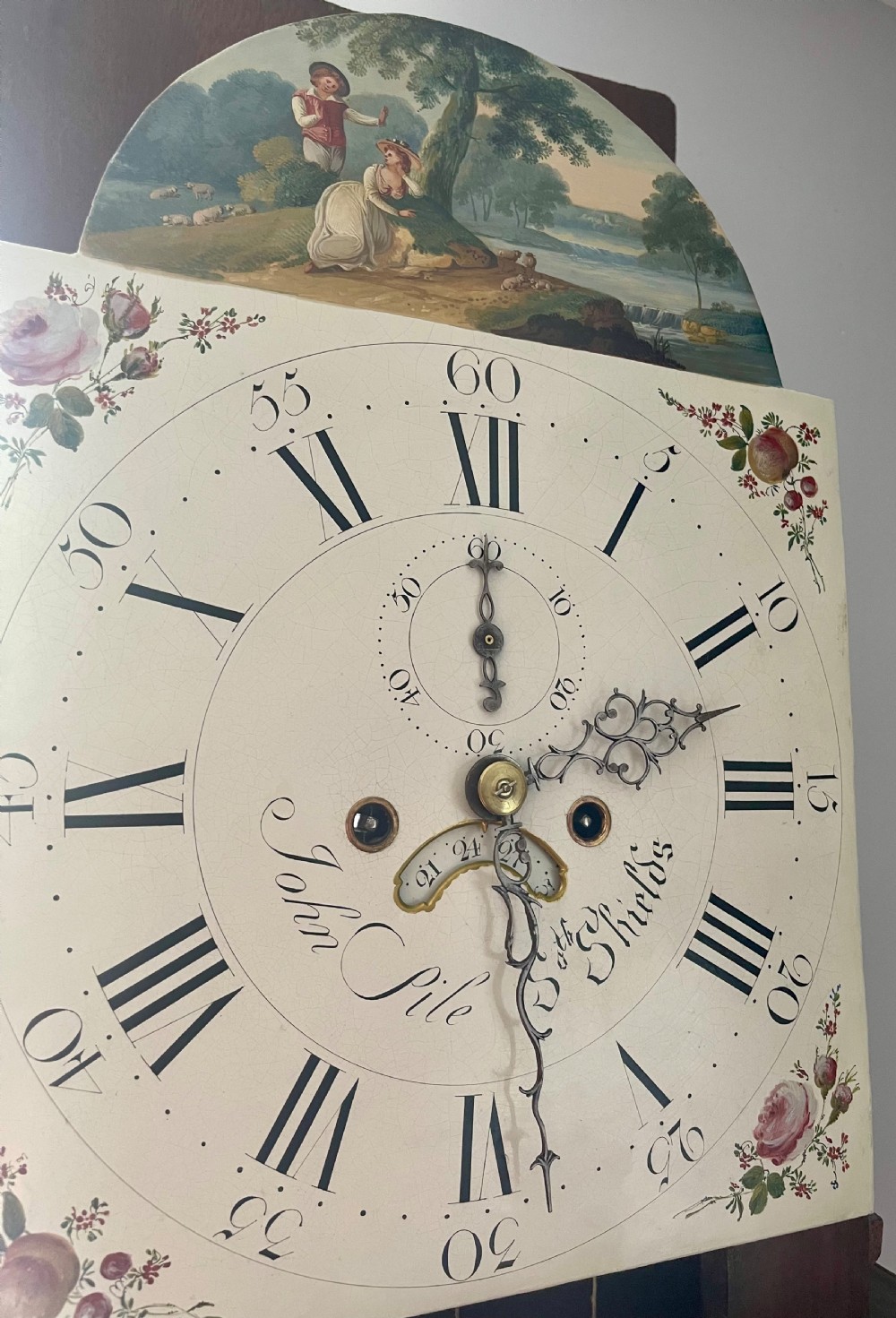 A Georgian oak longcase clock featuring a fretwork pediment, brass finial, hand-painted dial with Roman numerals, and an arched waist door. View XIV