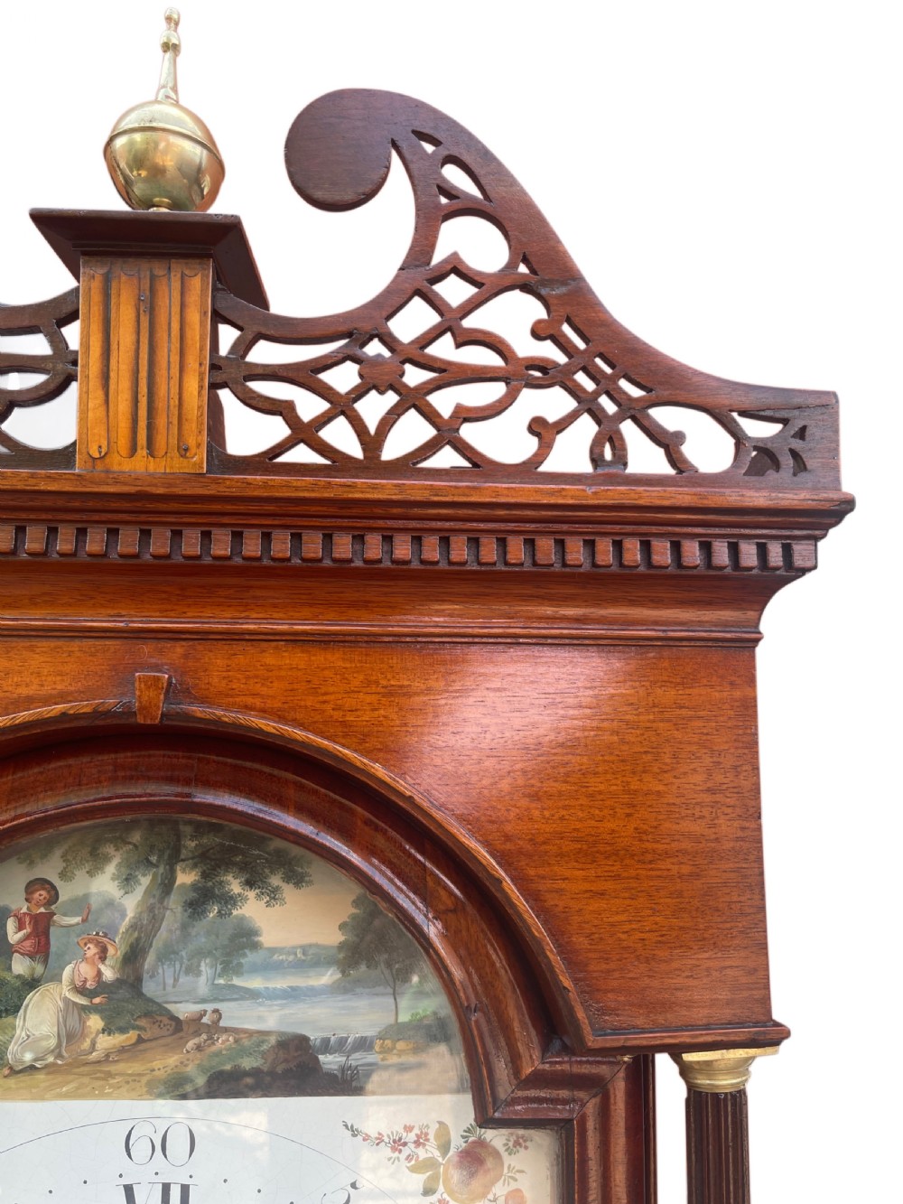 A Georgian oak longcase clock featuring a fretwork pediment, brass finial, hand-painted dial with Roman numerals, and an arched waist door. View XVI