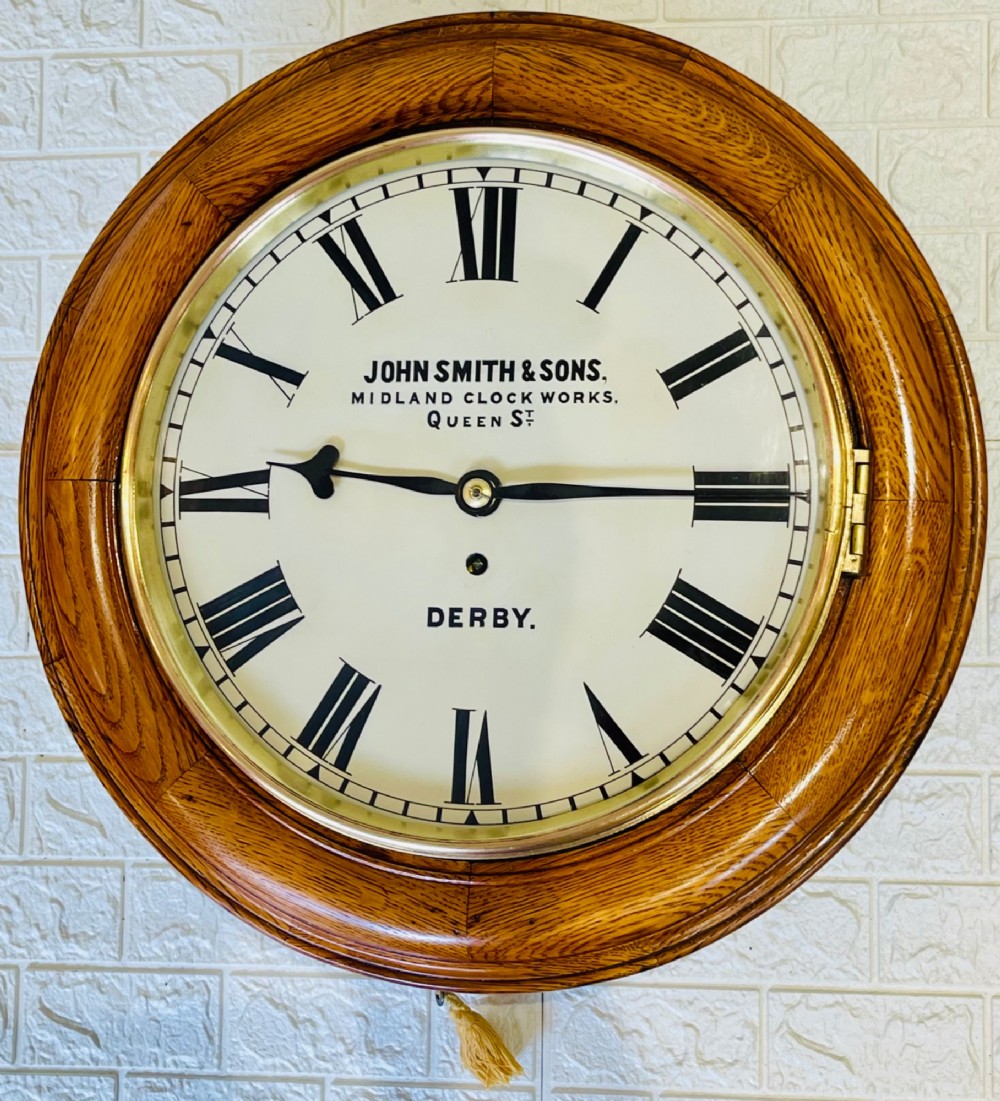 A circular antique oak wall clock featuring a white painted dial with black Roman numerals, brass bezel, and maker inscription. View III