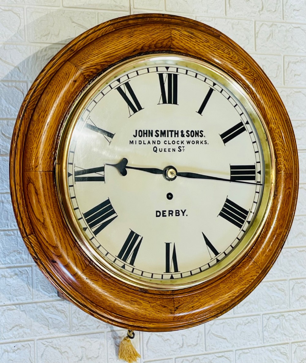 A circular antique oak wall clock featuring a white painted dial with black Roman numerals, brass bezel, and maker inscription. View IX