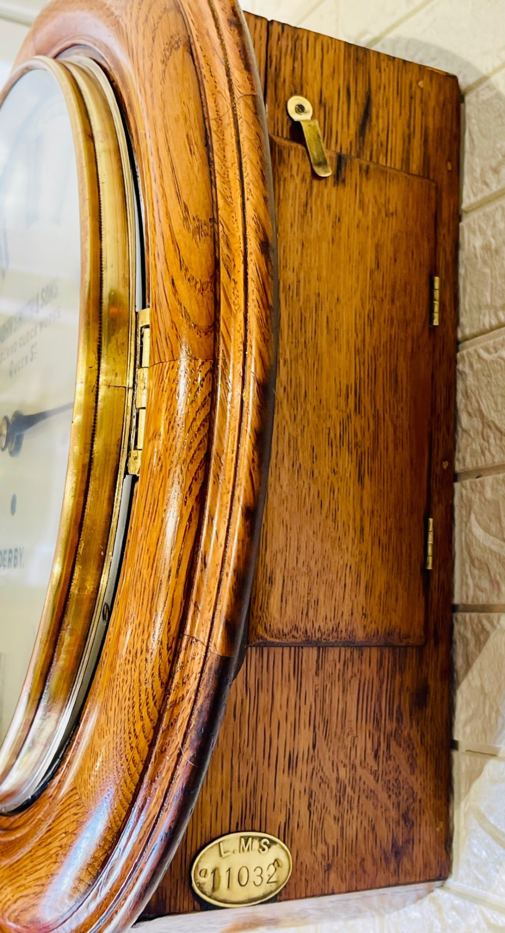 A circular antique oak wall clock featuring a white painted dial with black Roman numerals, brass bezel, and maker inscription. View XI