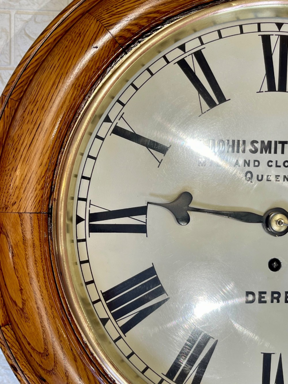 A circular antique oak wall clock featuring a white painted dial with black Roman numerals, brass bezel, and maker inscription. View XIII
