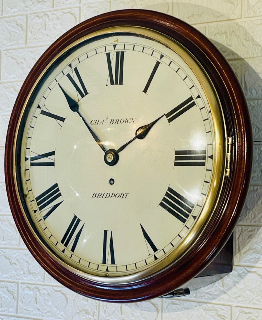 A circular Georgian fusee wall clock with a dark mahogany frame, a cream painted dial with Roman numerals, and a polished brass bezel.