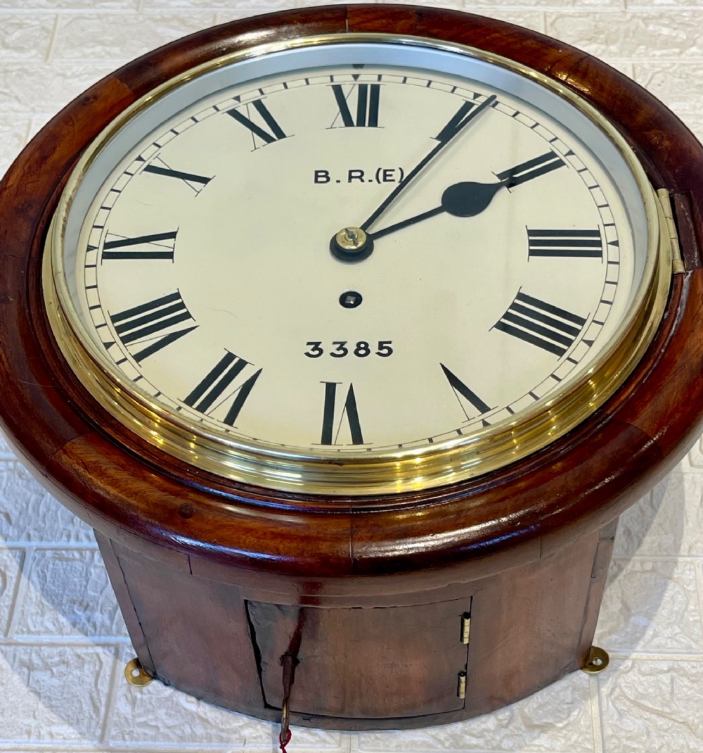 A circular antique mahogany railway dial wall clock with a painted off-white face, Roman numerals, brass bezel, and British Railways marking. View IV