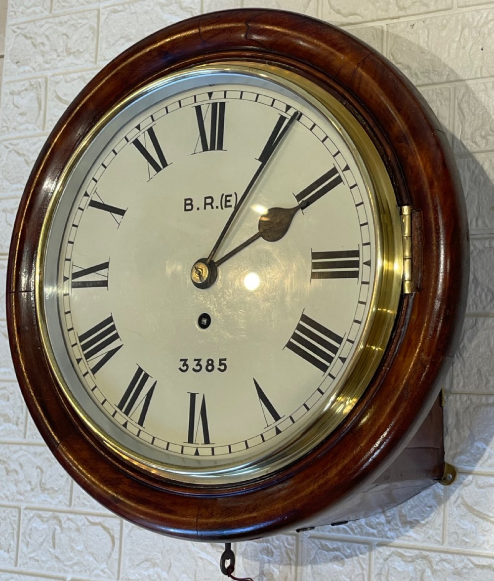 A circular antique mahogany railway dial wall clock with a painted off-white face, Roman numerals, brass bezel, and British Railways marking. View V