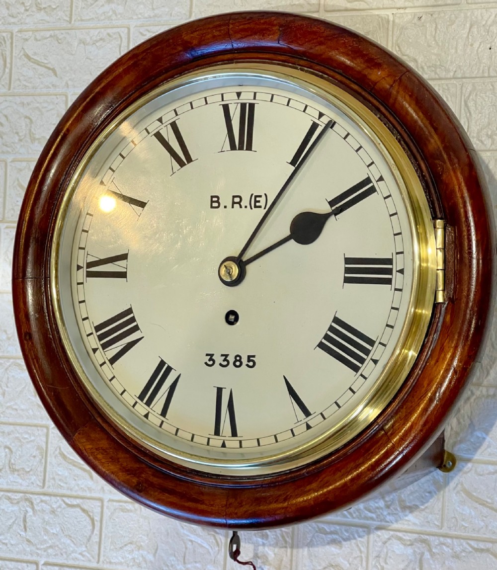 A circular antique mahogany railway dial wall clock with a painted off-white face, Roman numerals, brass bezel, and British Railways marking. View VI