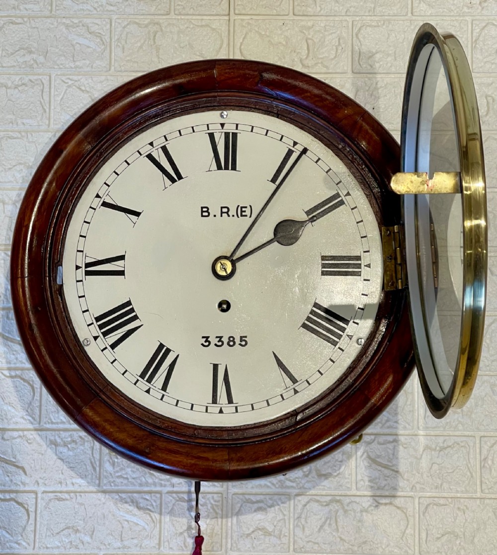 A circular antique mahogany railway dial wall clock with a painted off-white face, Roman numerals, brass bezel, and British Railways marking. View IX