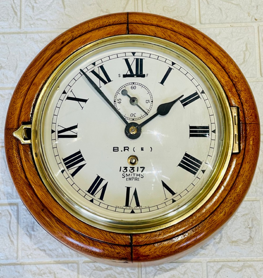 A circular vintage British Rail wall clock featuring a warm brown wooden casing, a hinged brass bezel, and a white dial with black Roman numerals stamped B.R.(E) Smiths Empire.