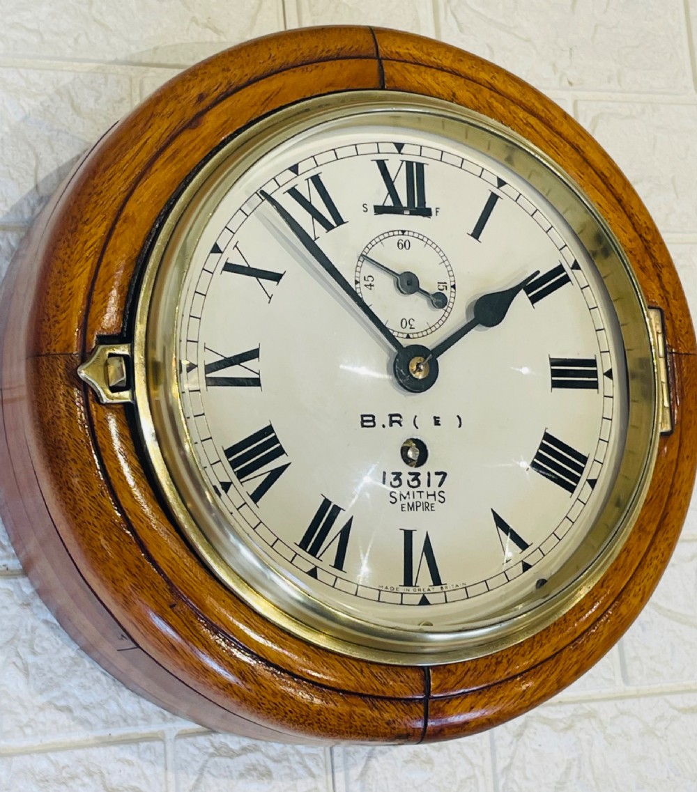 A circular vintage British Rail wall clock featuring a warm brown wooden casing, a hinged brass bezel, and a white dial with black Roman numerals stamped B.R.(E) Smiths Empire. View III