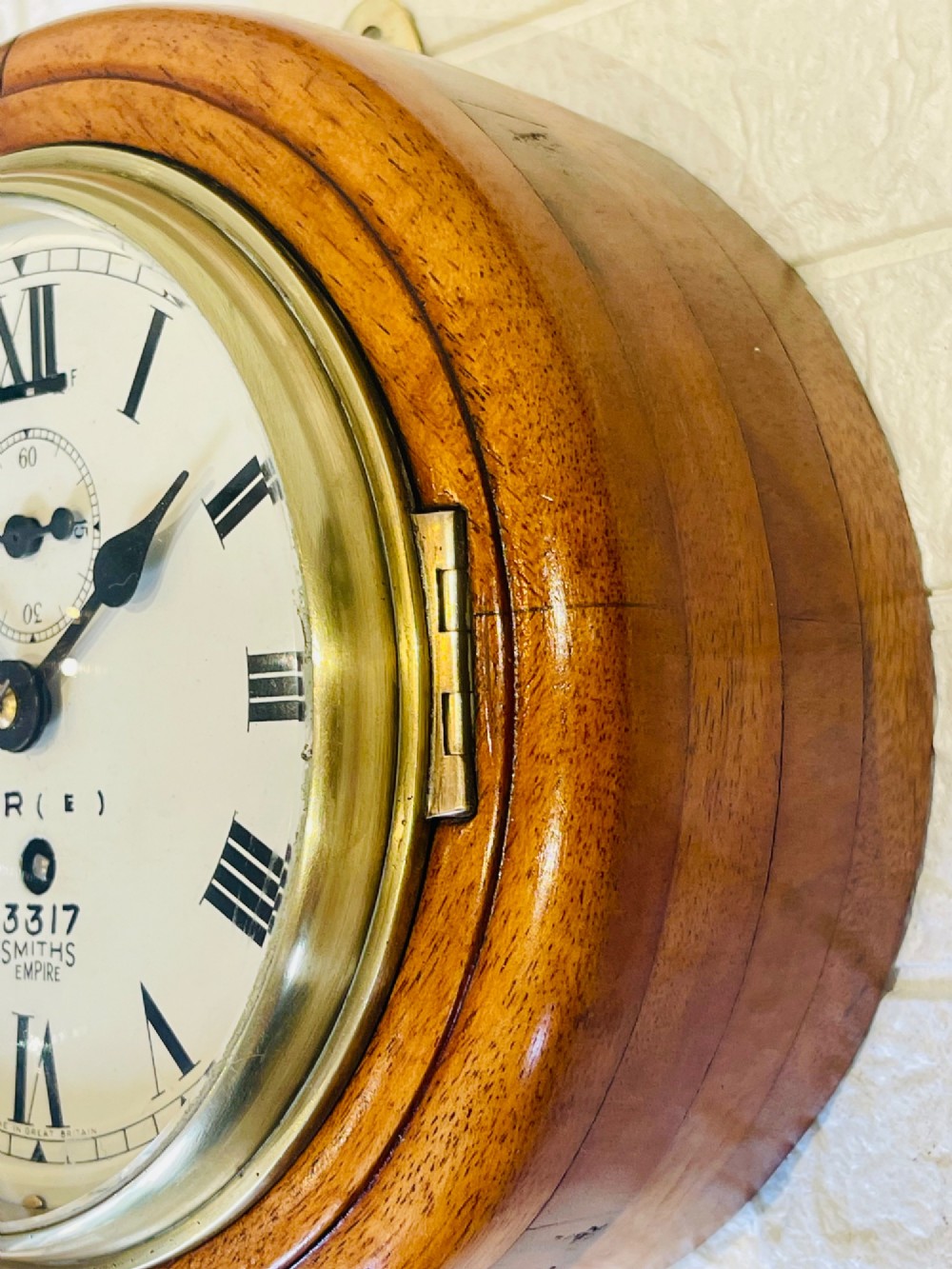 A circular vintage British Rail wall clock featuring a warm brown wooden casing, a hinged brass bezel, and a white dial with black Roman numerals stamped B.R.(E) Smiths Empire. View IV