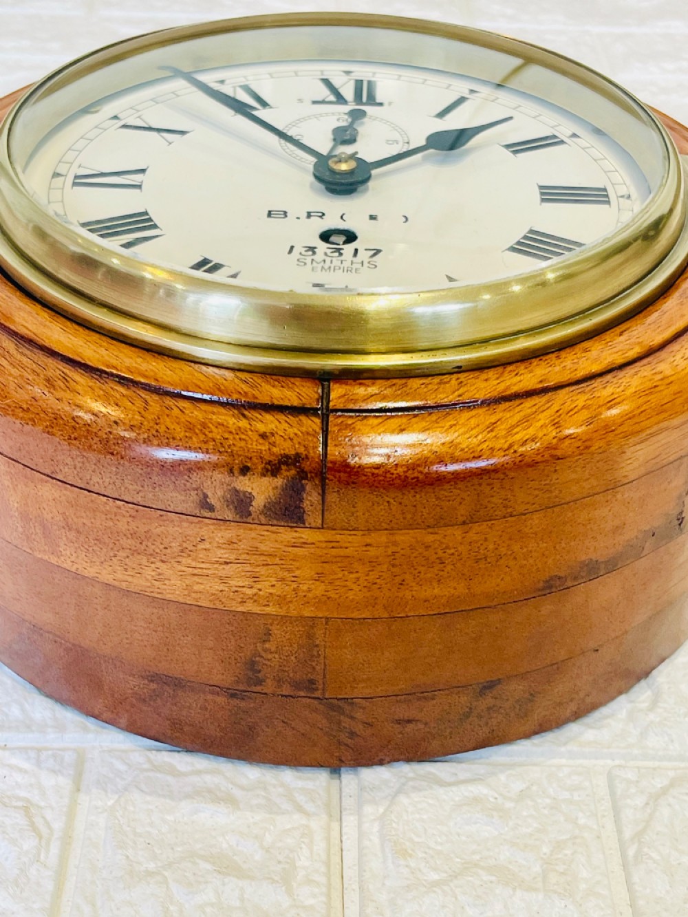 A circular vintage British Rail wall clock featuring a warm brown wooden casing, a hinged brass bezel, and a white dial with black Roman numerals stamped B.R.(E) Smiths Empire. View VII