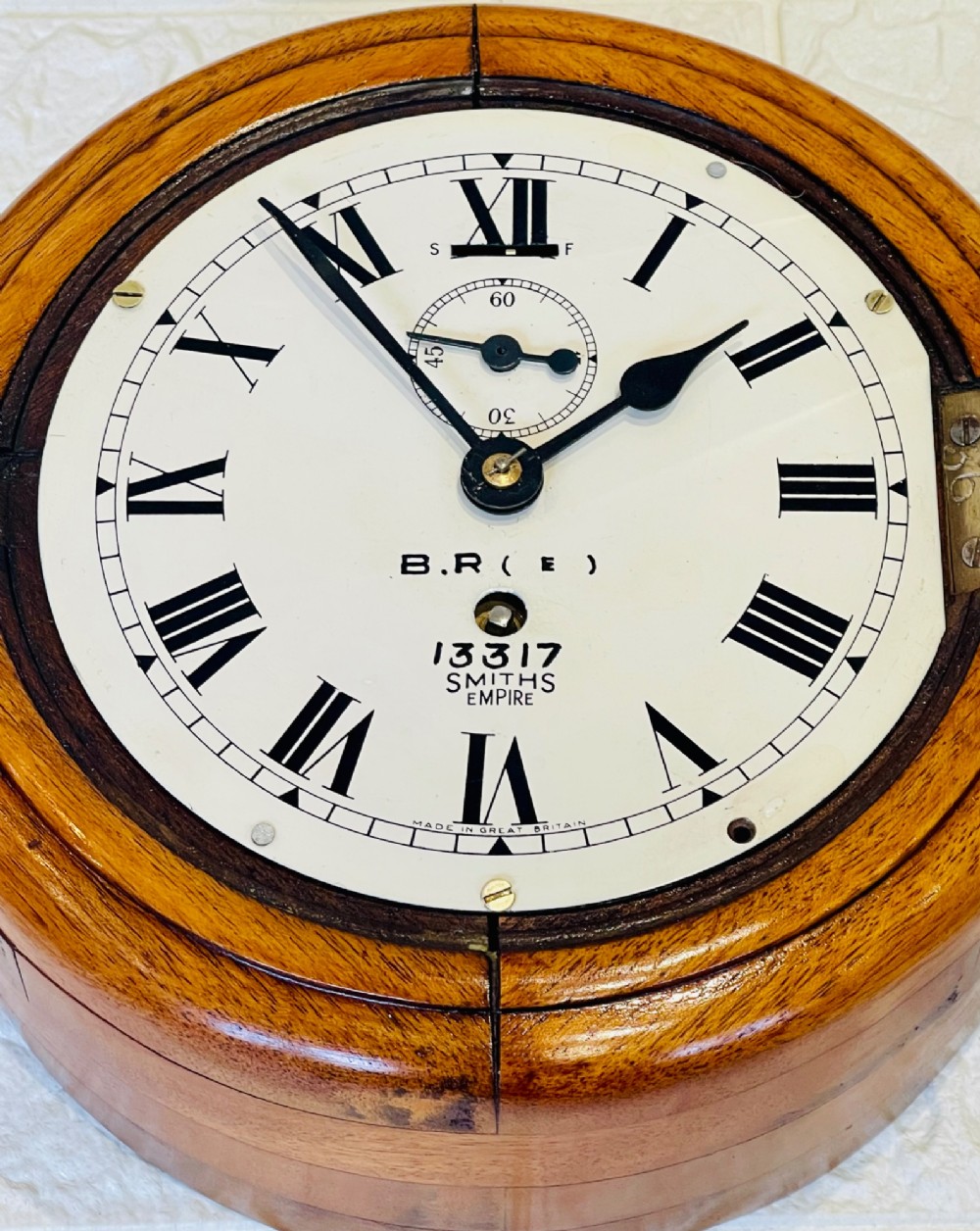 A circular vintage British Rail wall clock featuring a warm brown wooden casing, a hinged brass bezel, and a white dial with black Roman numerals stamped B.R.(E) Smiths Empire. View XII