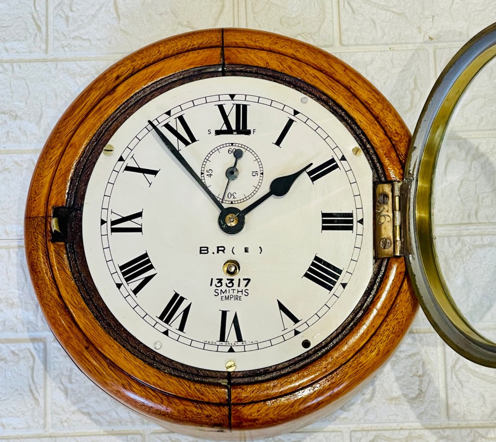 A circular vintage British Rail wall clock featuring a warm brown wooden casing, a hinged brass bezel, and a white dial with black Roman numerals stamped B.R.(E) Smiths Empire. View XIV