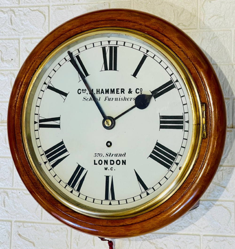 A circular Victorian mahogany wall clock featuring a white dial with black Roman numerals, a polished brass bezel, and London maker inscription.