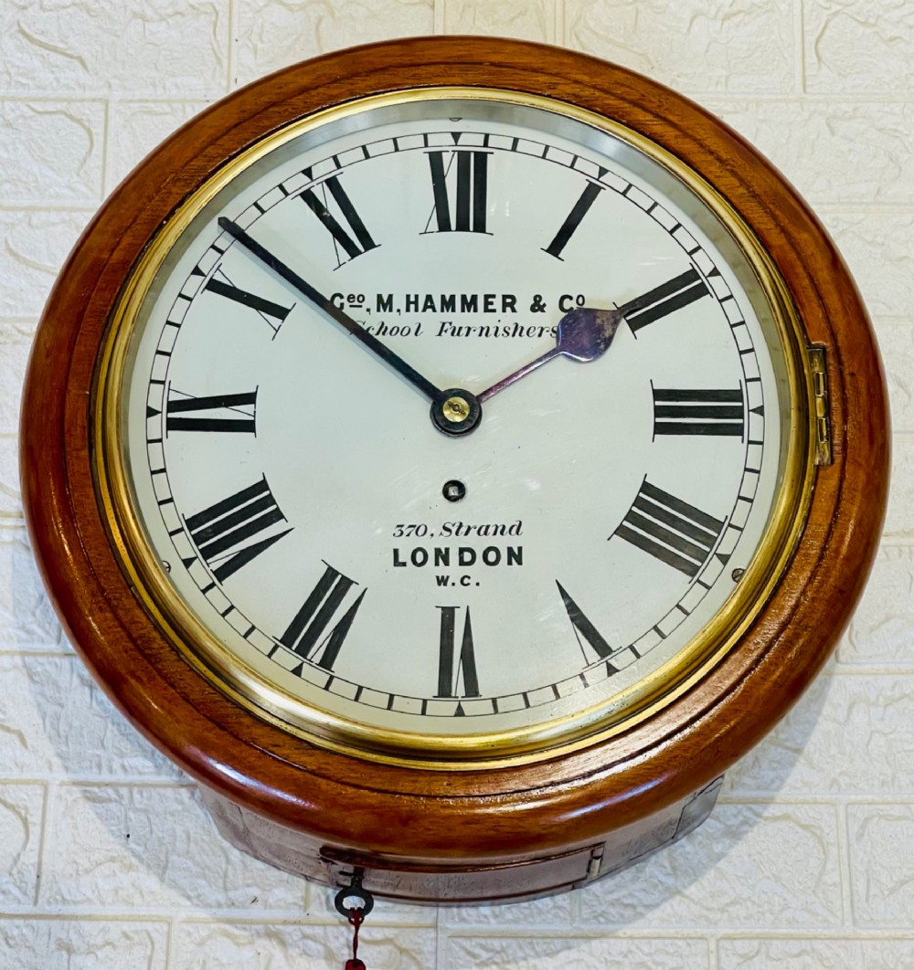 A circular Victorian mahogany wall clock featuring a white dial with black Roman numerals, a polished brass bezel, and London maker inscription. View IV