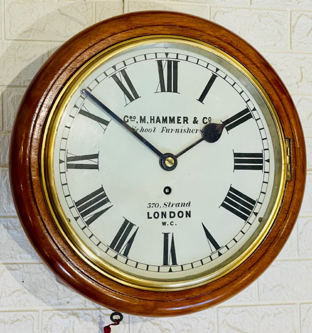 A circular Victorian mahogany wall clock featuring a white dial with black Roman numerals, a polished brass bezel, and London maker inscription. View V