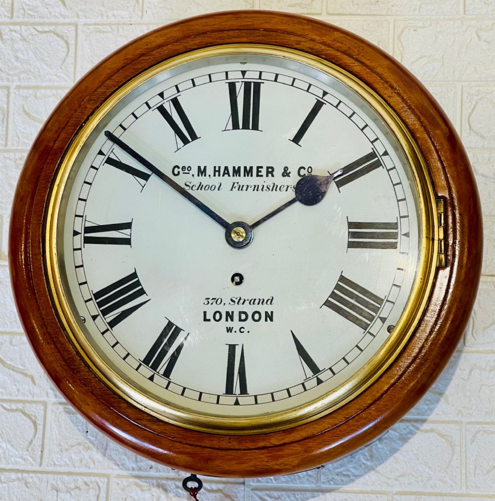 A circular Victorian mahogany wall clock featuring a white dial with black Roman numerals, a polished brass bezel, and London maker inscription. View VI