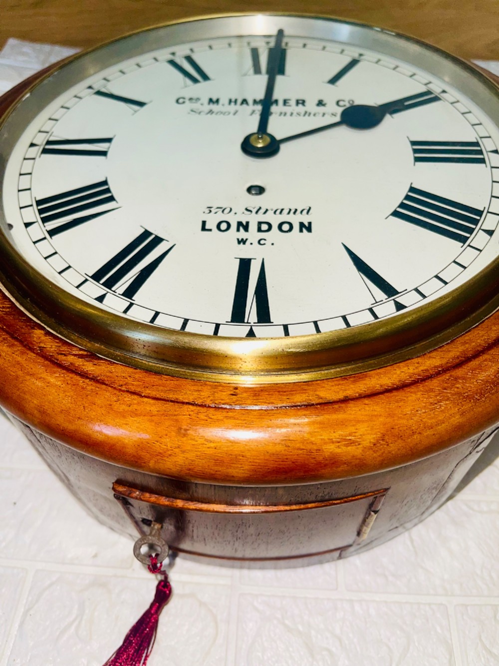 A circular Victorian mahogany wall clock featuring a white dial with black Roman numerals, a polished brass bezel, and London maker inscription. View VII