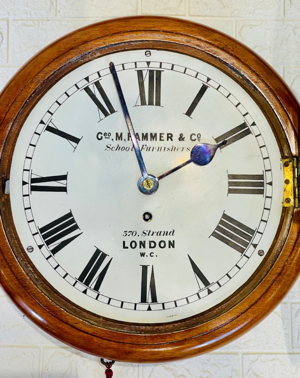 A circular Victorian mahogany wall clock featuring a white dial with black Roman numerals, a polished brass bezel, and London maker inscription. View IX