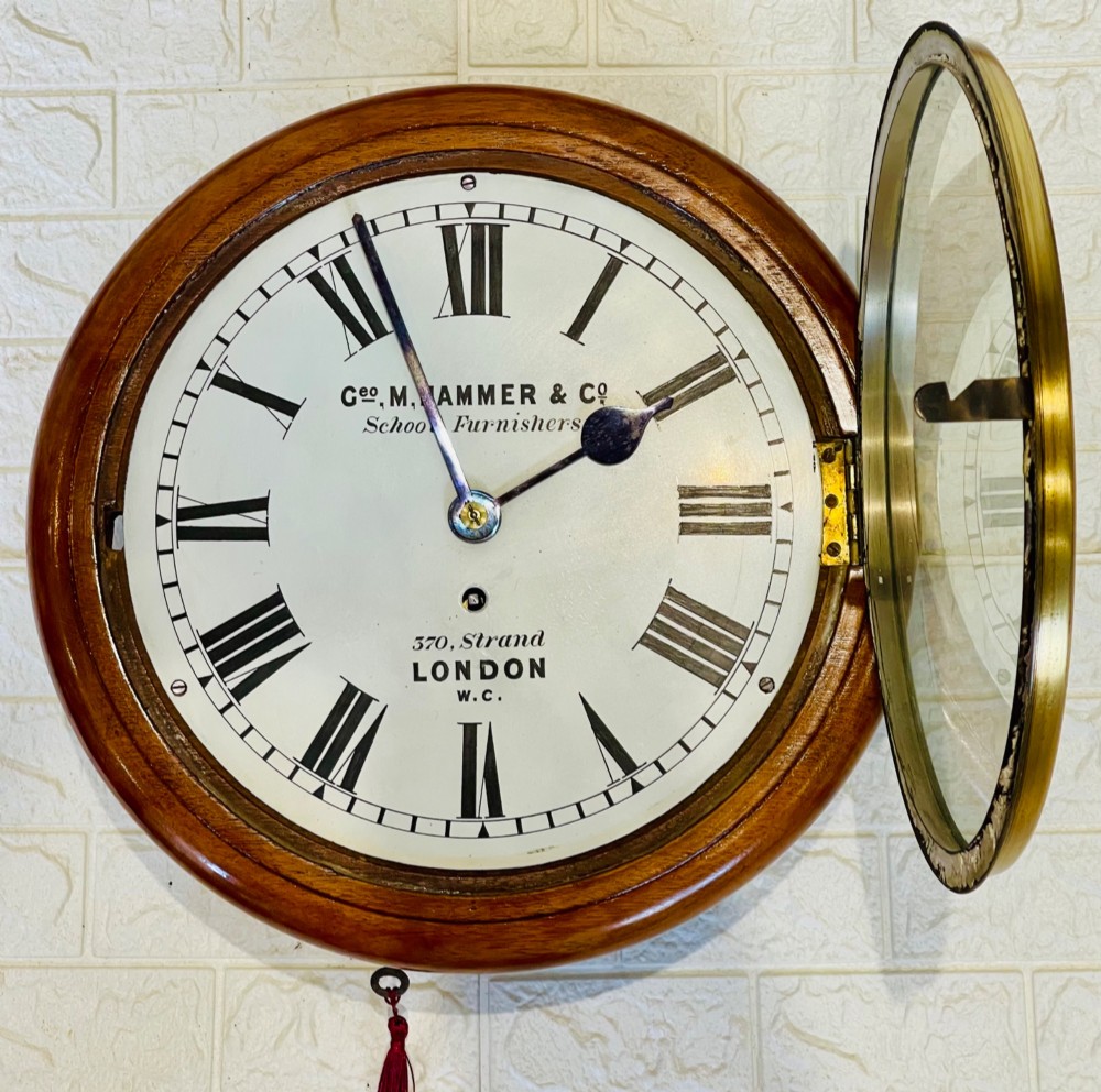 A circular Victorian mahogany wall clock featuring a white dial with black Roman numerals, a polished brass bezel, and London maker inscription. View X