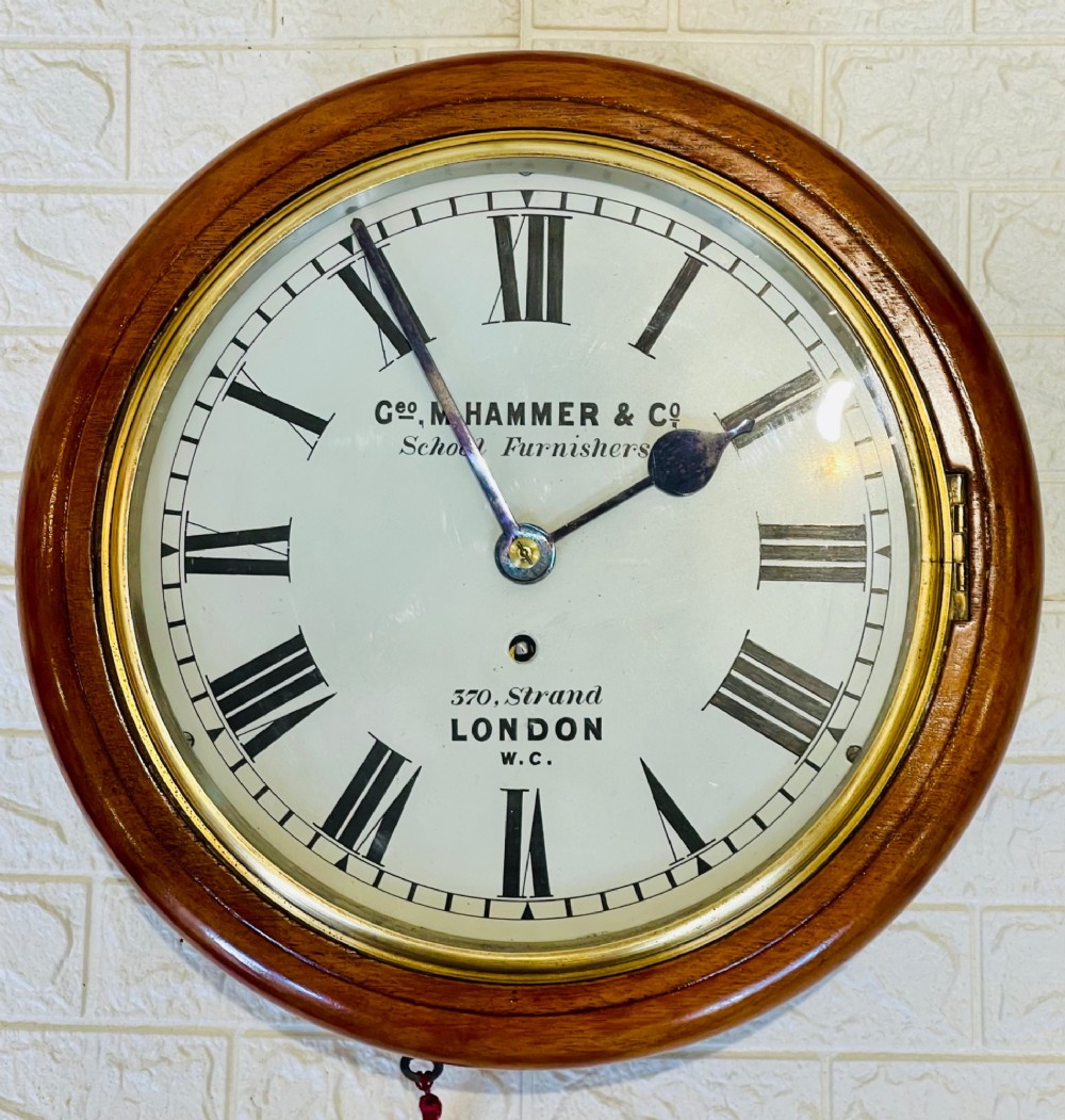 A circular Victorian mahogany wall clock featuring a white dial with black Roman numerals, a polished brass bezel, and London maker inscription. View XII