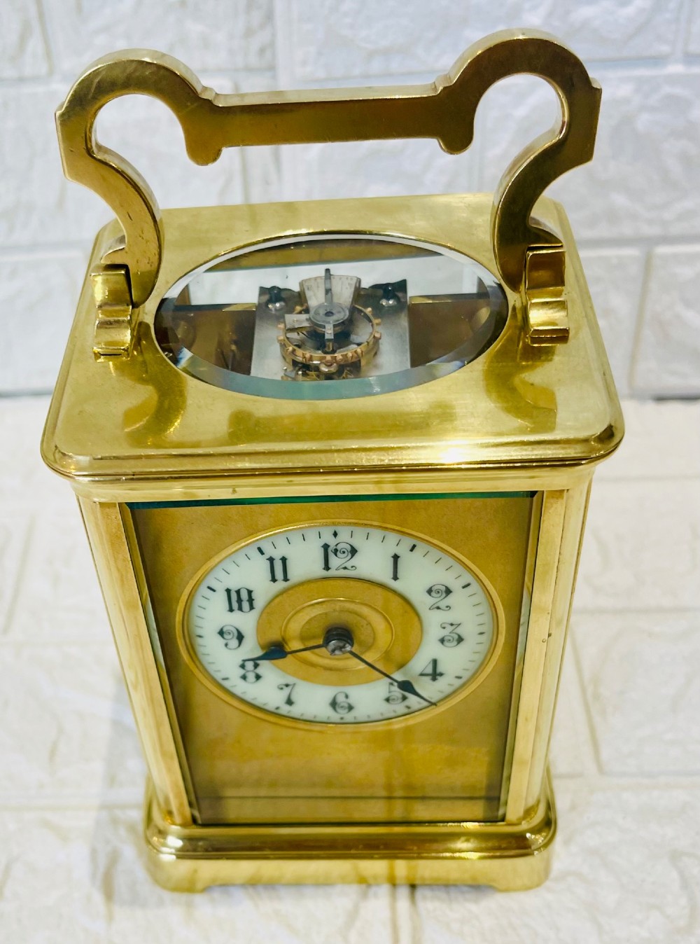 A French brass carriage clock featuring a top carrying handle, clear glass viewing panels, and a white enamel dial with black numerals. View IV