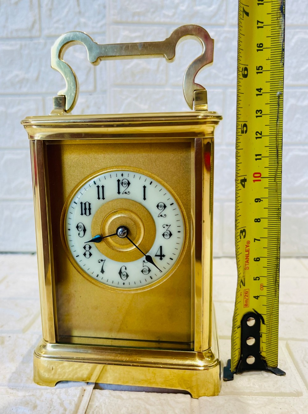 A French brass carriage clock featuring a top carrying handle, clear glass viewing panels, and a white enamel dial with black numerals. View V