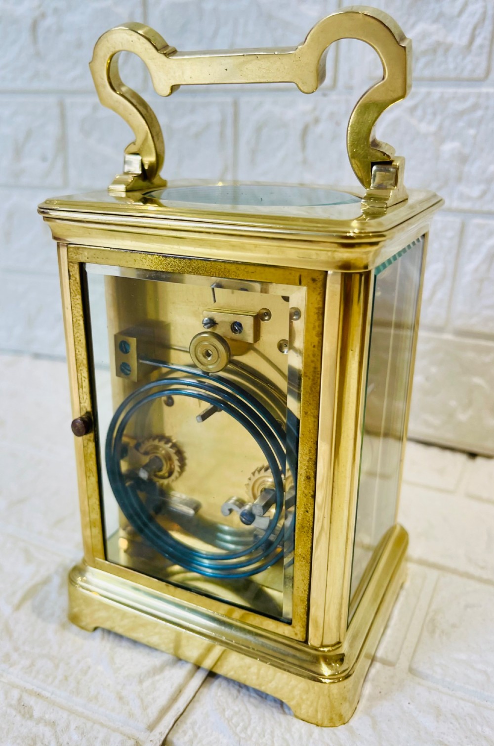 A French brass carriage clock featuring a top carrying handle, clear glass viewing panels, and a white enamel dial with black numerals. View X