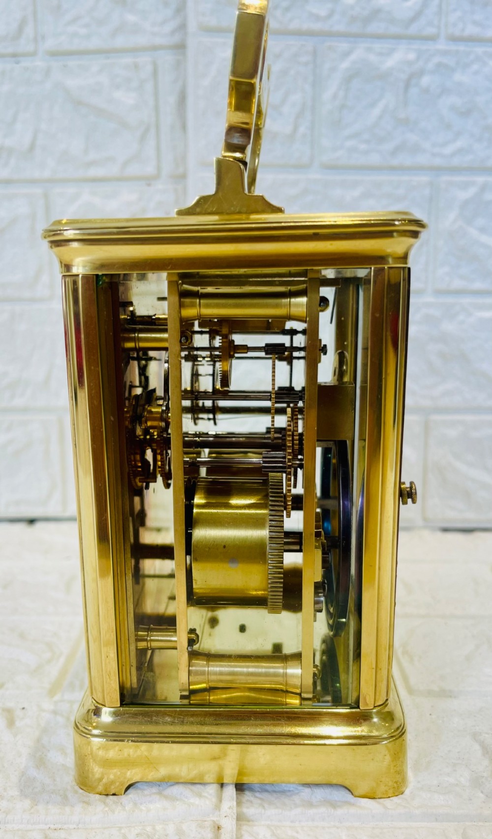 A French brass carriage clock featuring a top carrying handle, clear glass viewing panels, and a white enamel dial with black numerals. View XII