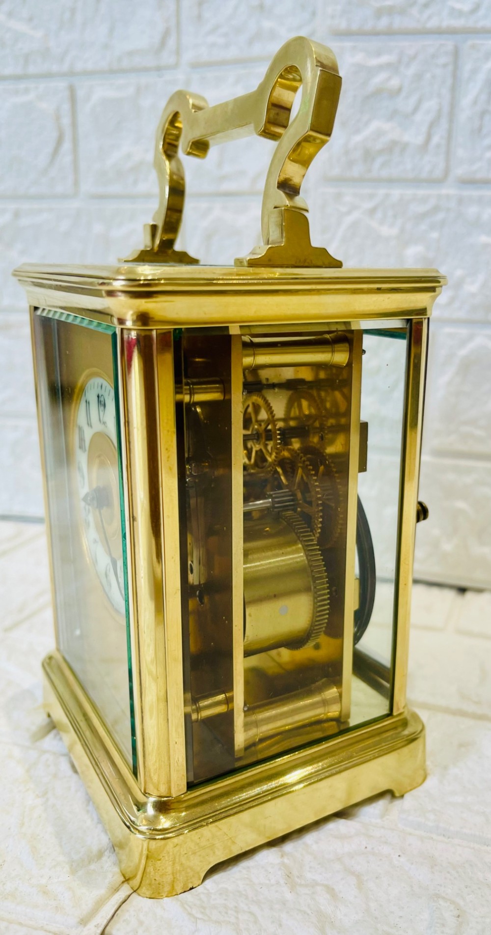 A French brass carriage clock featuring a top carrying handle, clear glass viewing panels, and a white enamel dial with black numerals. View XIII