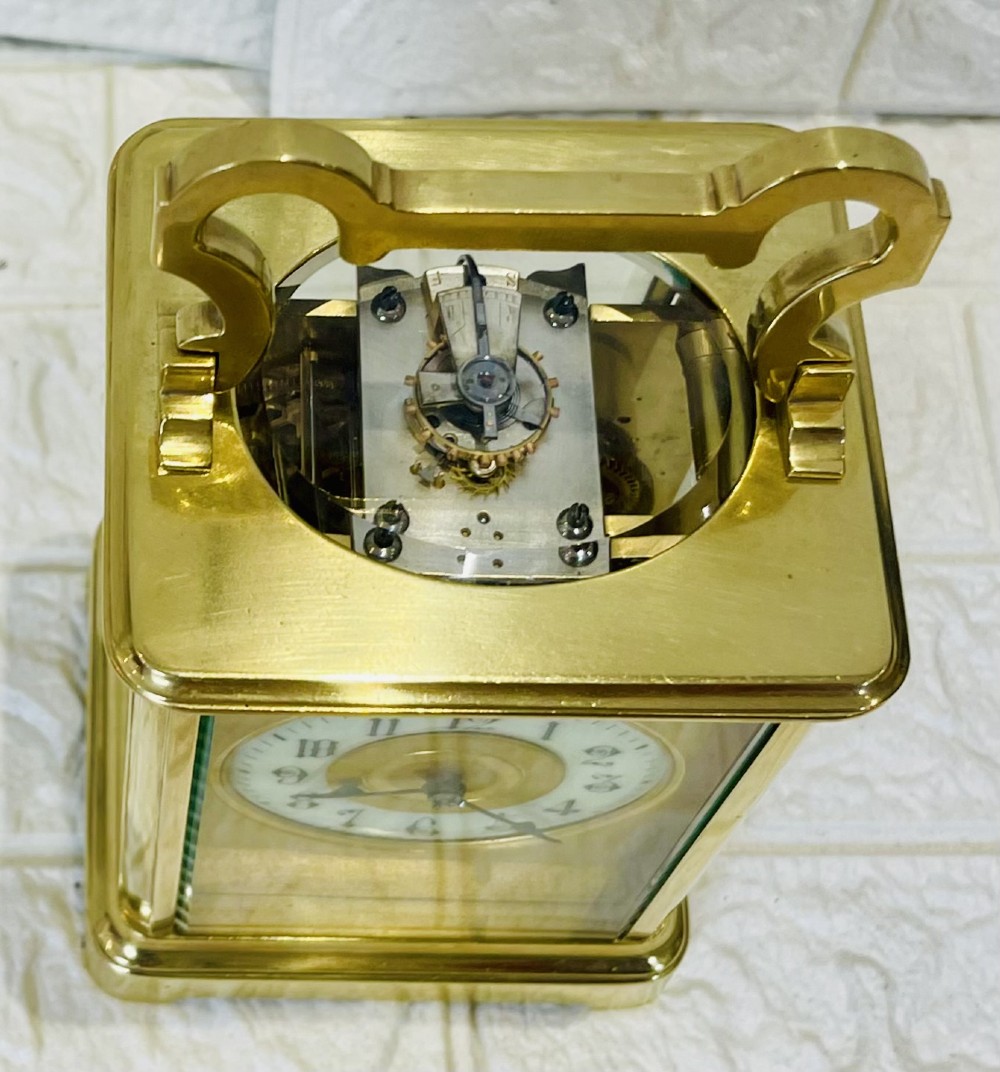 A French brass carriage clock featuring a top carrying handle, clear glass viewing panels, and a white enamel dial with black numerals. View XIV