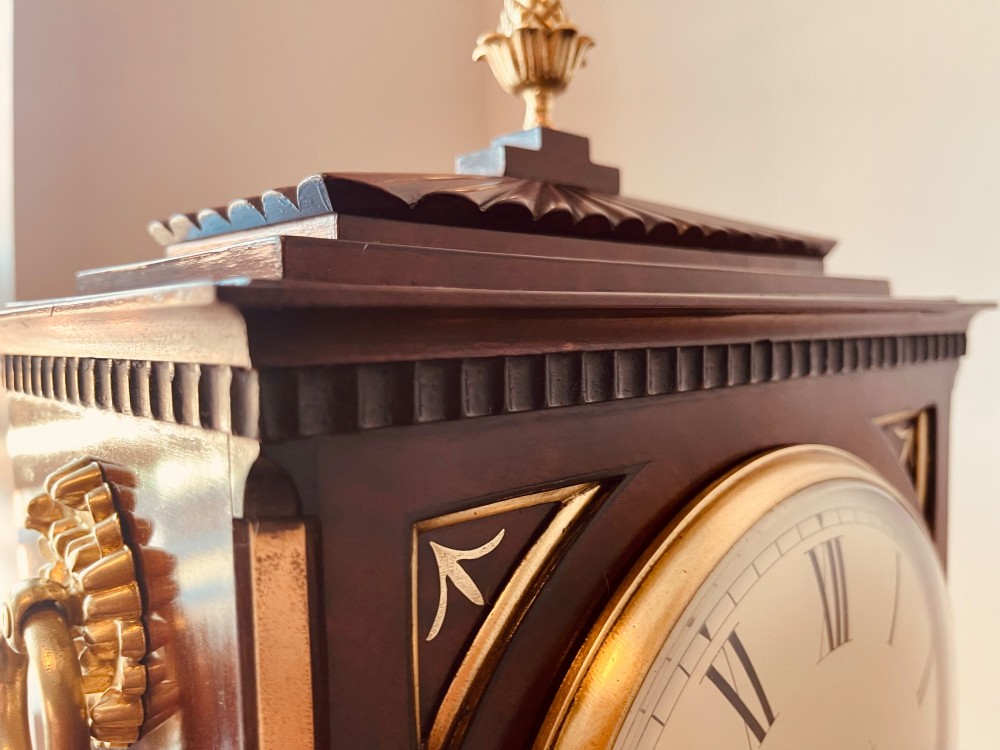 An antique Regency dark mahogany bracket clock featuring intricate brass inlay scrollwork, a brass pineapple finial, side brass lion-mask drop handles, and a cream dial with Roman numerals. View III