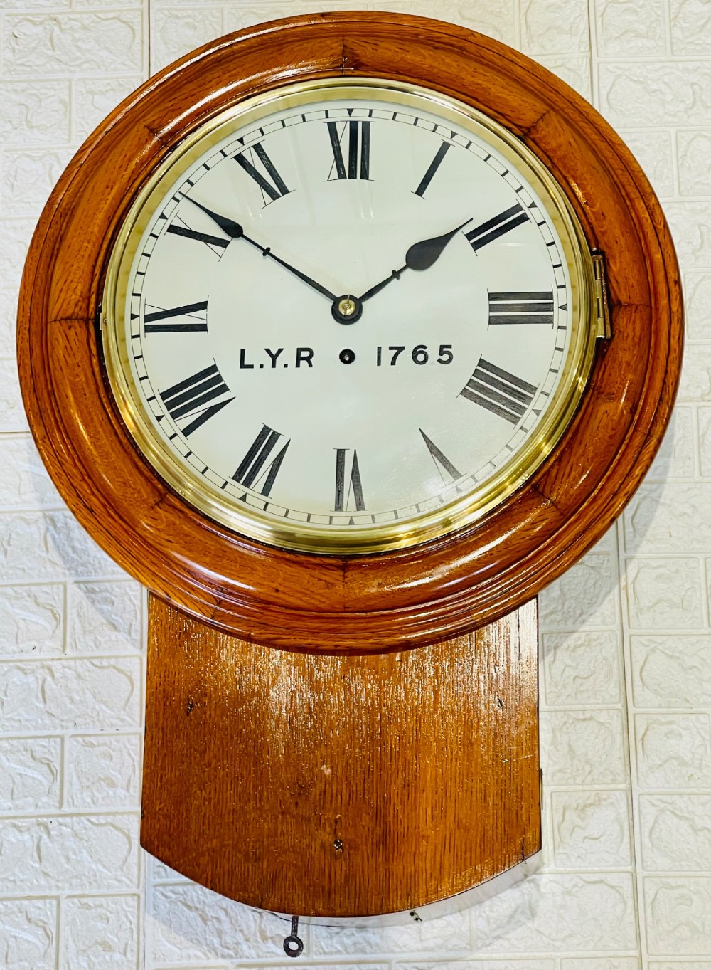 An antique oak drop dial wall clock featuring a white face with Roman numerals, marked L.Y.R 1765 with a brass bezel.