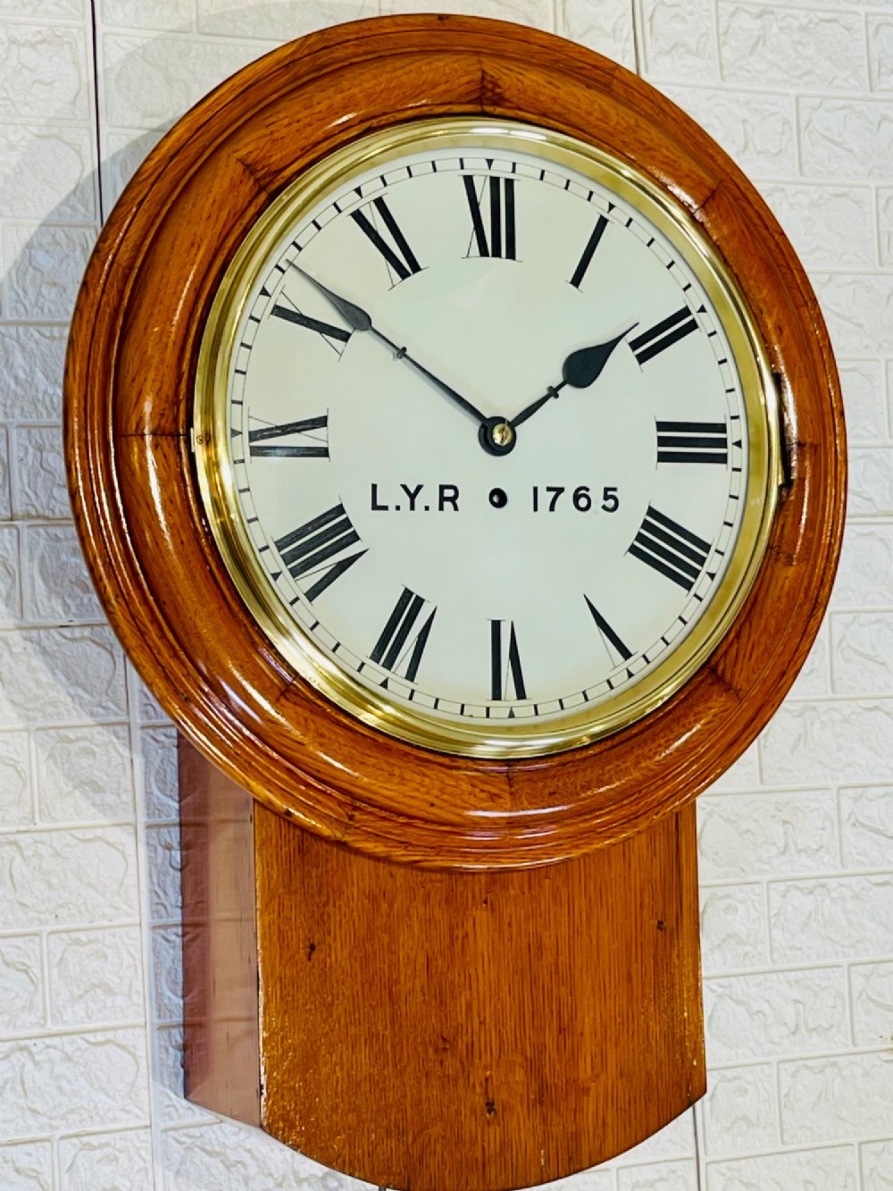 An antique oak drop dial wall clock featuring a white face with Roman numerals, marked L.Y.R 1765 with a brass bezel. View II
