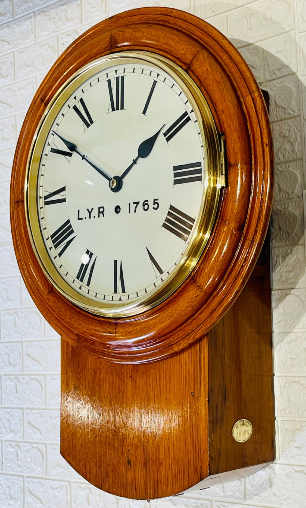 An antique oak drop dial wall clock featuring a white face with Roman numerals, marked L.Y.R 1765 with a brass bezel. View V
