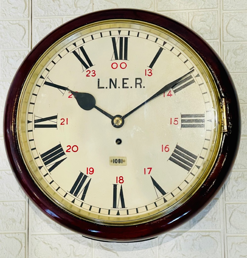 A circular LNER fusee railway wall clock featuring a dark mahogany wooden surround, brass bezel, cream dial with black Roman numerals and red 24-hour numbers.
