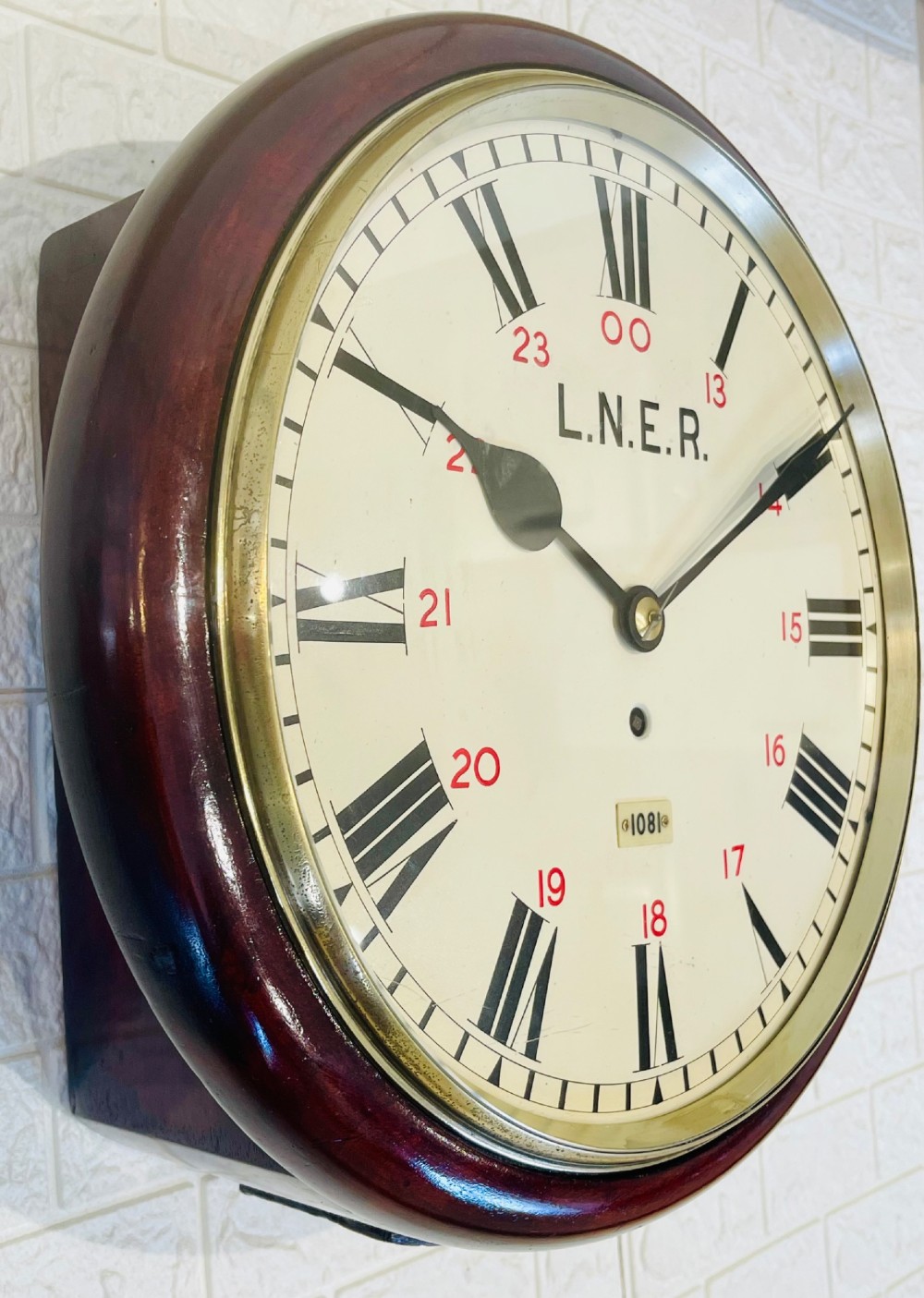A circular LNER fusee railway wall clock featuring a dark mahogany wooden surround, brass bezel, cream dial with black Roman numerals and red 24-hour numbers. View II