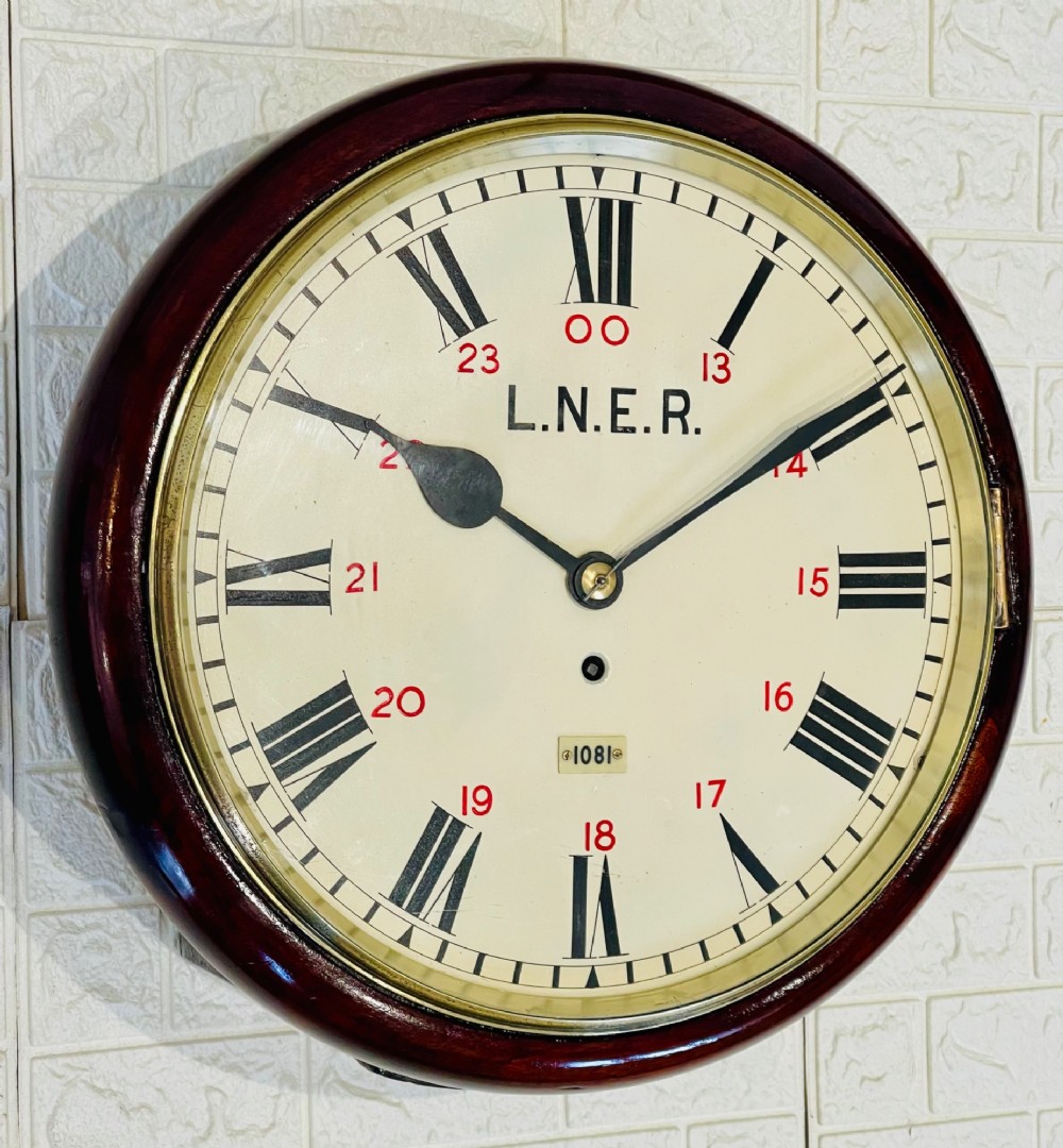 A circular LNER fusee railway wall clock featuring a dark mahogany wooden surround, brass bezel, cream dial with black Roman numerals and red 24-hour numbers. View IV