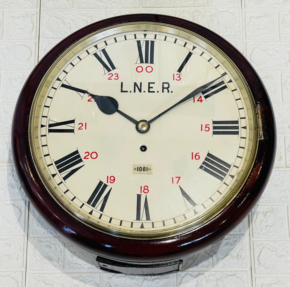 A circular LNER fusee railway wall clock featuring a dark mahogany wooden surround, brass bezel, cream dial with black Roman numerals and red 24-hour numbers. View VI