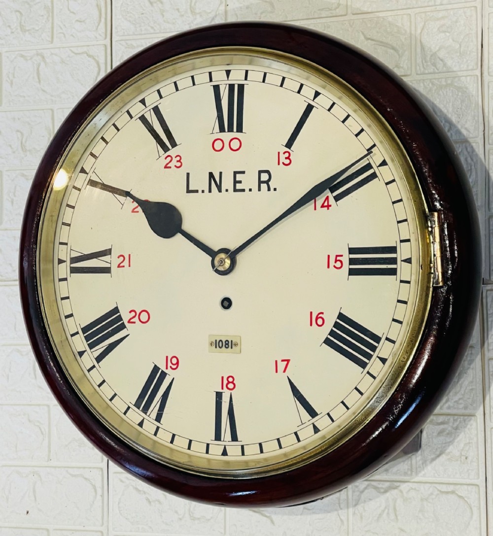 A circular LNER fusee railway wall clock featuring a dark mahogany wooden surround, brass bezel, cream dial with black Roman numerals and red 24-hour numbers. View VII