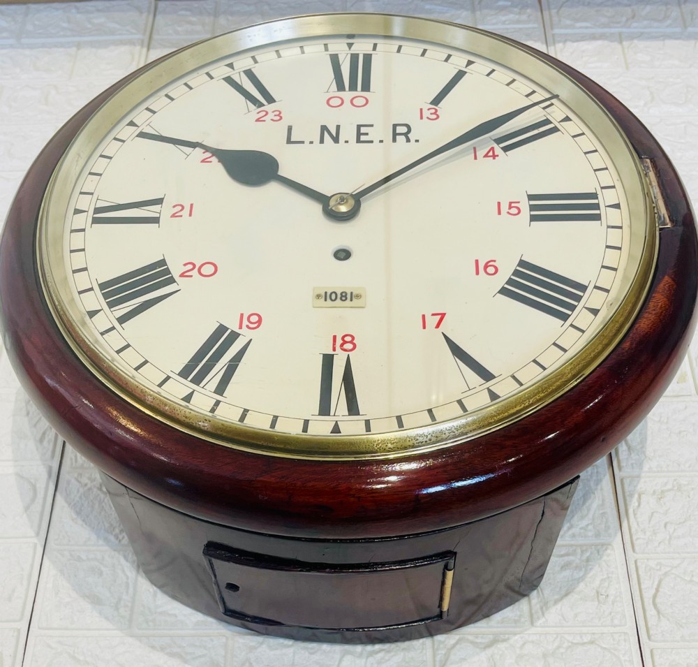 A circular LNER fusee railway wall clock featuring a dark mahogany wooden surround, brass bezel, cream dial with black Roman numerals and red 24-hour numbers. View XIV