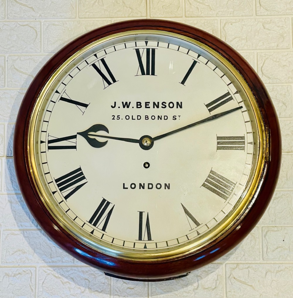 A circular mahogany fusee wall clock featuring a white dial face with black Roman numerals, brass bezel, and J. W. Benson London markings.